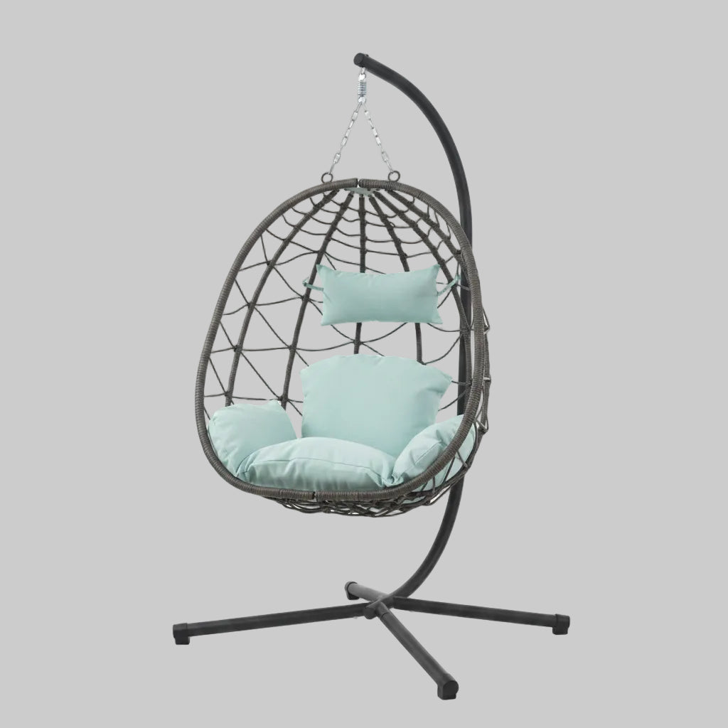 Luxury indoor and outdoor hanging egg chair with a black powder-coated steel stand and plush gray cushions on a sunlit patio.