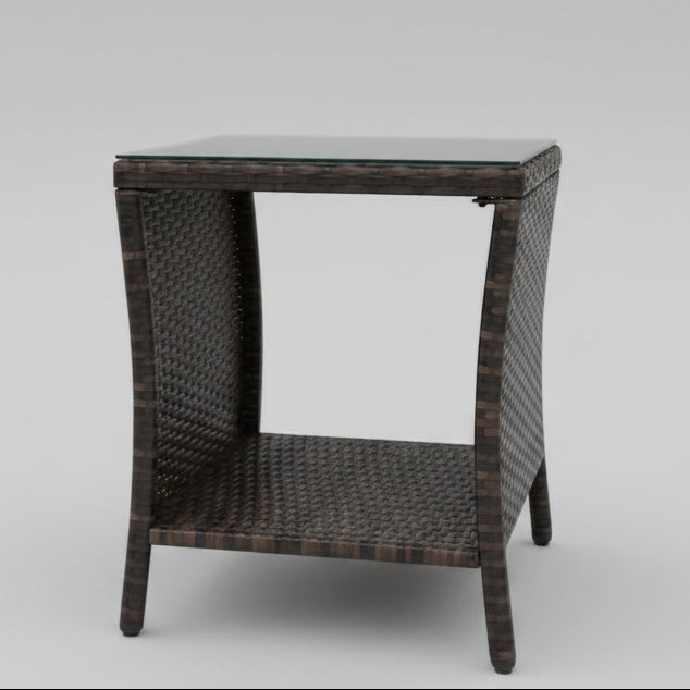 Modern brown PE rattan wicker outdoor coffee table featuring a sleek, transparent tempered glass top on a sunny garden patio.